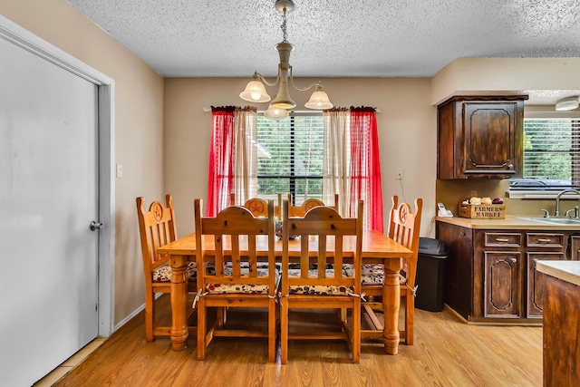 dining area with a chandelier, a textured ceiling, light hardwood / wood-style floors, and sink