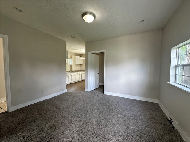 unfurnished bedroom with a textured ceiling, dark carpet, and ensuite bathroom