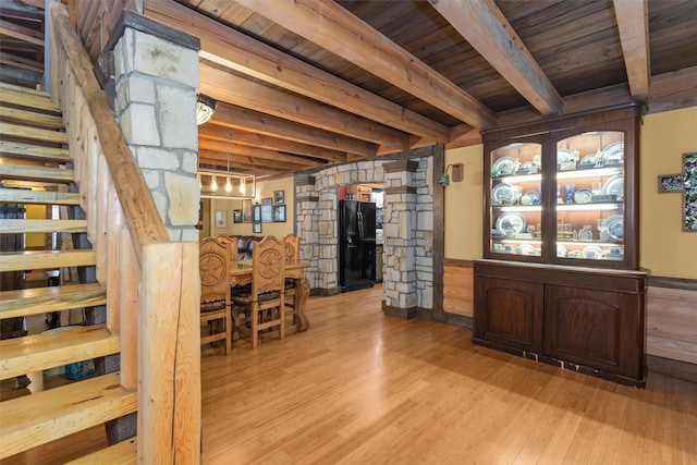 bar with light hardwood / wood-style flooring, beamed ceiling, black refrigerator with ice dispenser, hanging light fixtures, and wooden ceiling