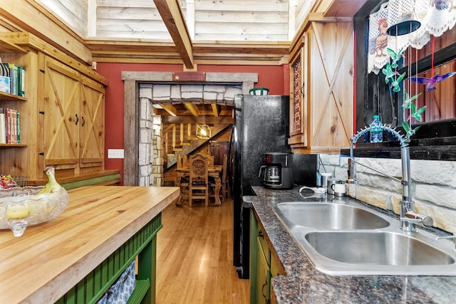 kitchen featuring beam ceiling, light hardwood / wood-style floors, sink, and black refrigerator