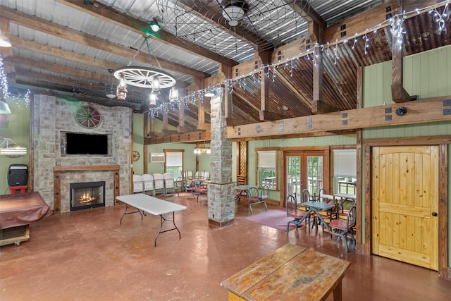 living room with a stone fireplace, concrete floors, beamed ceiling, and french doors