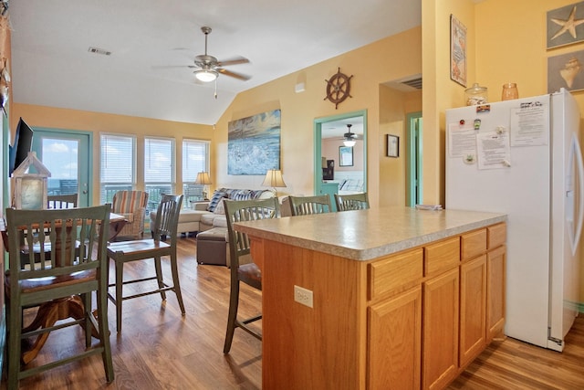 kitchen with a breakfast bar area, ceiling fan, white refrigerator with ice dispenser, vaulted ceiling, and light wood-type flooring