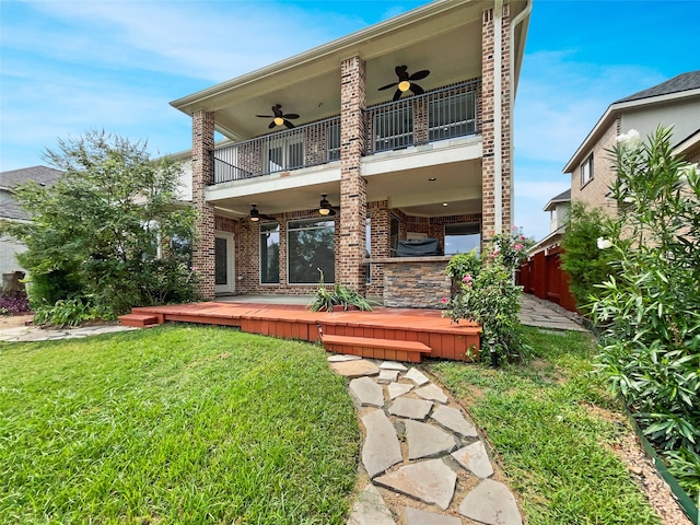 back of property with a balcony, ceiling fan, and a yard