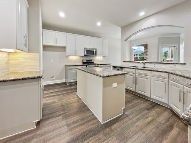 kitchen featuring white cabinets, a center island, stone counters, stainless steel appliances, and sink