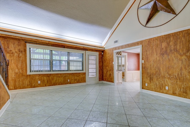 tiled spare room featuring ornamental molding, lofted ceiling, a textured ceiling, and wooden walls