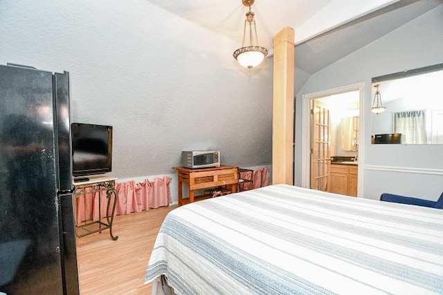 bedroom featuring vaulted ceiling, ensuite bathroom, black refrigerator, and hardwood / wood-style floors