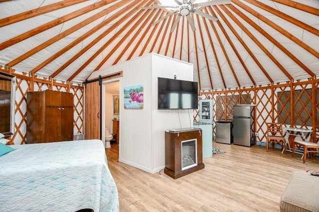 bedroom featuring a barn door, vaulted ceiling with beams, light wood-type flooring, and stainless steel refrigerator