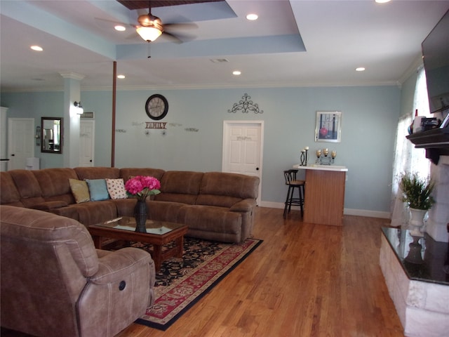 living room with hardwood / wood-style flooring, ornamental molding, ceiling fan, and a raised ceiling