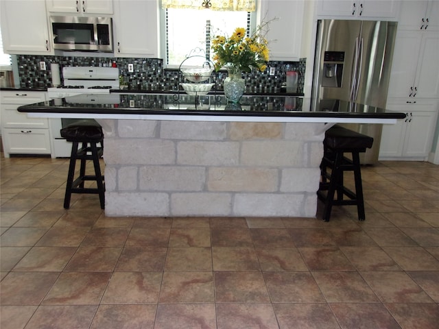 kitchen featuring white cabinetry, stainless steel appliances, backsplash, a kitchen bar, and dark tile floors