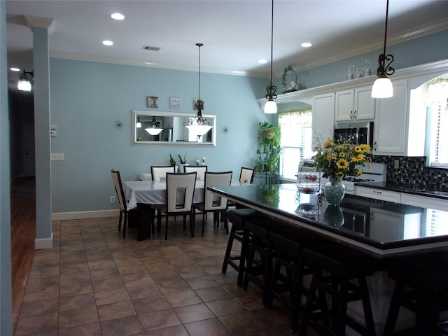 kitchen featuring decorative light fixtures, backsplash, white cabinetry, dark tile flooring, and a breakfast bar