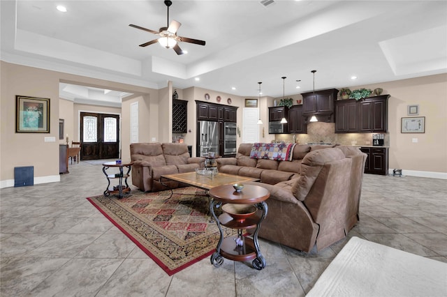 living room with a raised ceiling, ceiling fan, and french doors