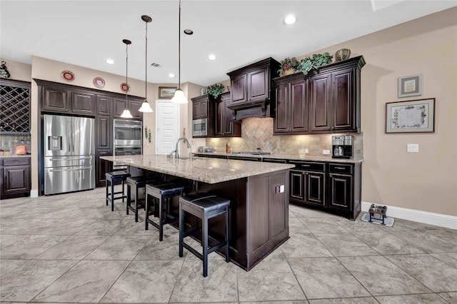 kitchen with dark brown cabinetry, stainless steel appliances, sink, hanging light fixtures, and an island with sink