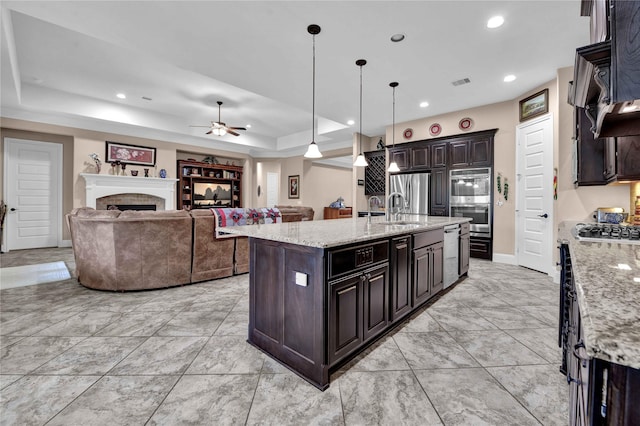 kitchen with dark brown cabinetry, a raised ceiling, ceiling fan, decorative light fixtures, and an island with sink