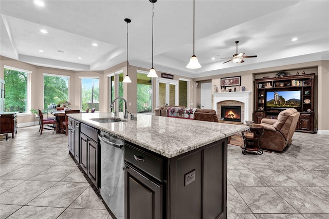 kitchen with a raised ceiling, sink, stainless steel dishwasher, an island with sink, and decorative light fixtures