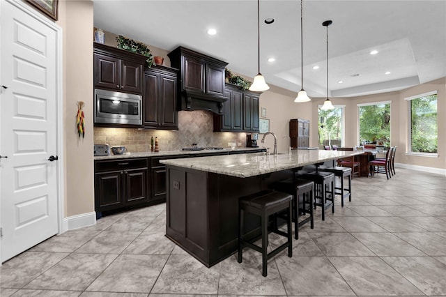 kitchen with appliances with stainless steel finishes, dark brown cabinets, a raised ceiling, a spacious island, and hanging light fixtures