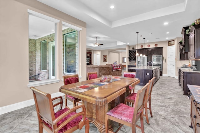 dining area featuring light tile patterned floors, a tray ceiling, ceiling fan, and sink