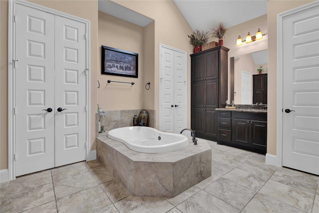 bathroom featuring vanity, a relaxing tiled tub, and vaulted ceiling