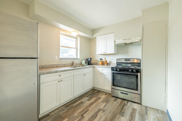 kitchen with light stone counters, stainless steel appliances, sink, hardwood / wood-style floors, and white cabinetry