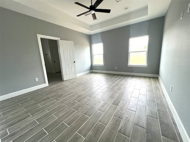 empty room with dark hardwood / wood-style floors, a tray ceiling, and ceiling fan