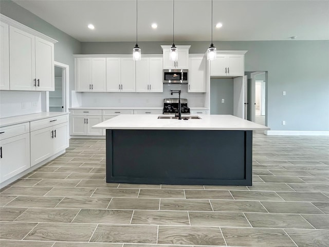 kitchen with a kitchen island with sink, a sink, light countertops, wood tiled floor, and stainless steel microwave