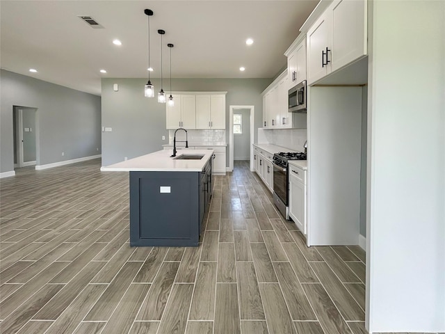 kitchen with wood finish floors, a sink, visible vents, range with gas stovetop, and stainless steel microwave