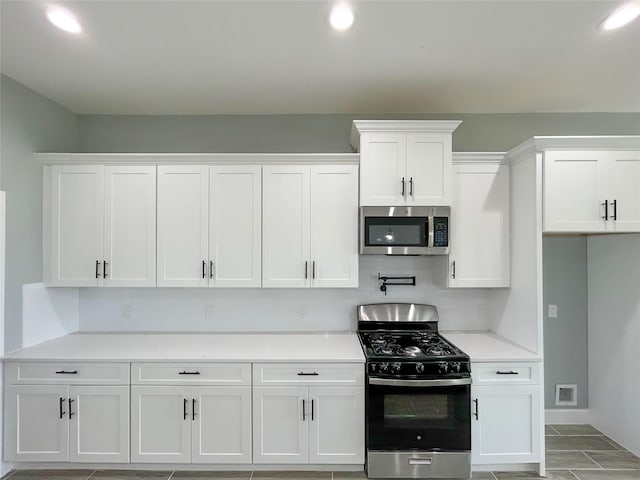 kitchen with white cabinetry, gas range oven, stainless steel microwave, and light countertops