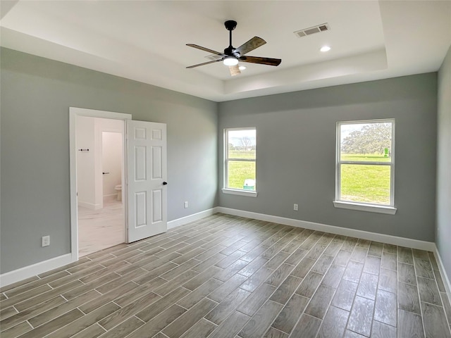 unfurnished room with a tray ceiling, visible vents, and baseboards