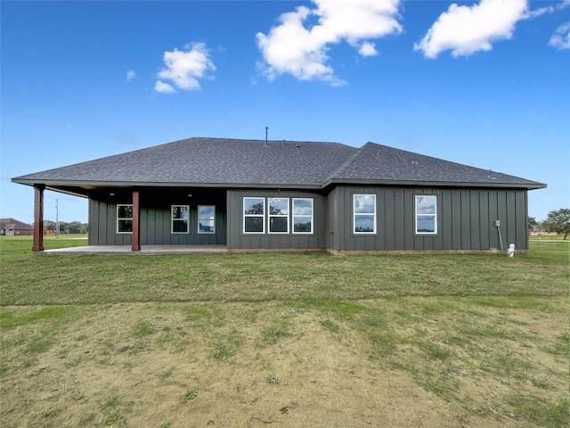 back of property with roof with shingles, board and batten siding, a patio, and a lawn