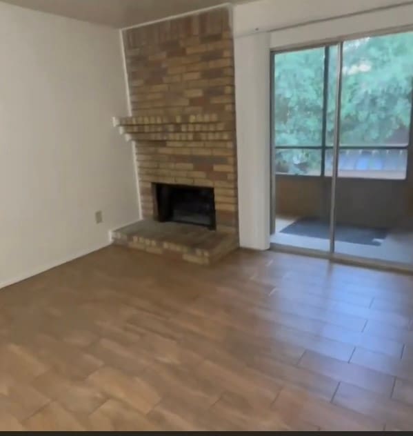 unfurnished living room featuring brick wall, a brick fireplace, and hardwood / wood-style floors