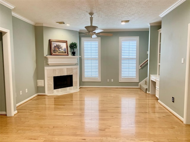 unfurnished living room featuring light hardwood / wood-style flooring, ceiling fan, ornamental molding, a textured ceiling, and a tiled fireplace