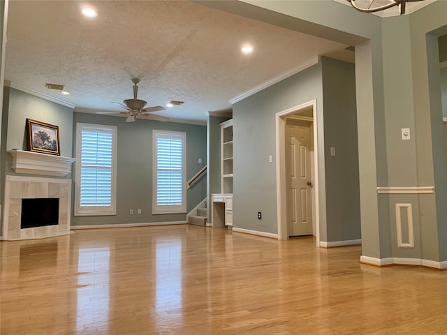 unfurnished living room featuring a tiled fireplace, crown molding, and light hardwood / wood-style flooring