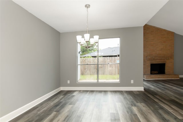 interior space featuring vaulted ceiling, a chandelier, a brick fireplace, brick wall, and dark wood-type flooring