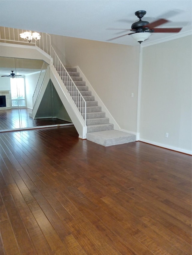 empty room with ceiling fan with notable chandelier, crown molding, and dark wood-type flooring