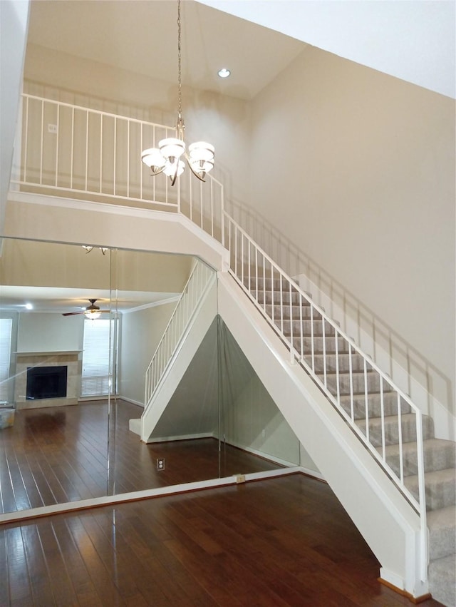 staircase featuring a high ceiling, ceiling fan with notable chandelier, and hardwood / wood-style floors