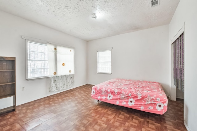 bedroom with parquet floors, a textured ceiling, and multiple windows