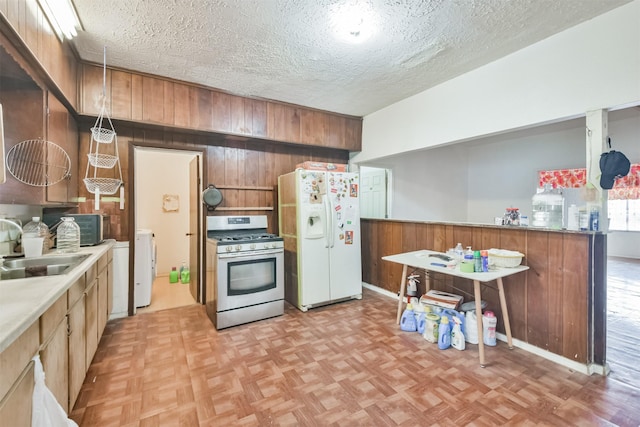 kitchen featuring white refrigerator with ice dispenser, sink, wooden walls, stainless steel gas stove, and washer / dryer