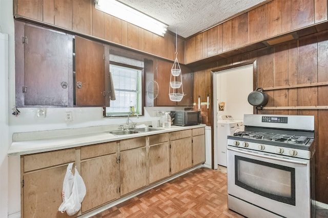 kitchen with gas range, sink, washing machine and dryer, wooden walls, and light parquet flooring