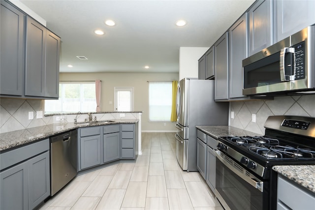 kitchen with appliances with stainless steel finishes, sink, gray cabinets, light stone countertops, and decorative backsplash