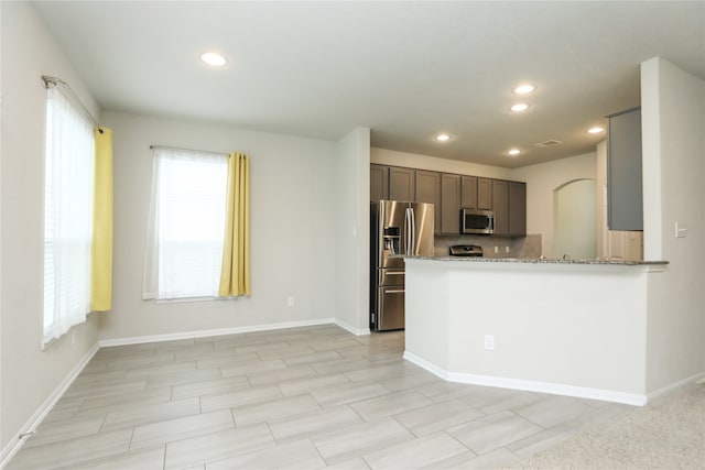 kitchen with appliances with stainless steel finishes, light stone counters, dark brown cabinets, and kitchen peninsula