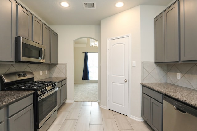 kitchen with appliances with stainless steel finishes, dark stone countertops, light colored carpet, and decorative backsplash