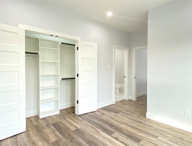 unfurnished bedroom with a closet, light hardwood / wood-style flooring, a barn door, and ensuite bathroom