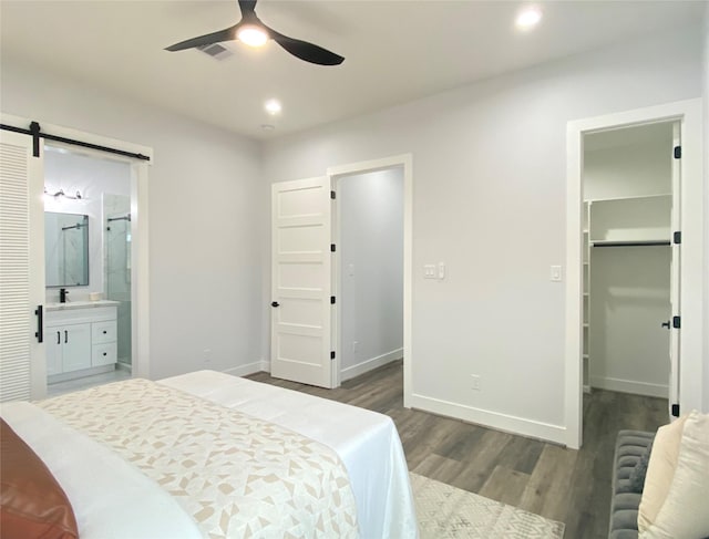 bedroom with a spacious closet, a barn door, dark wood-type flooring, ensuite bath, and a closet