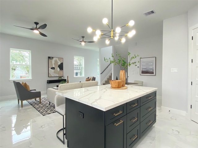 kitchen with a breakfast bar, hanging light fixtures, a center island, light stone counters, and ceiling fan with notable chandelier