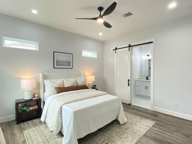 bedroom with multiple windows, wood-type flooring, a barn door, and connected bathroom