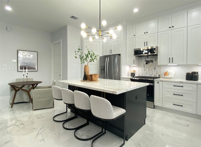 kitchen with appliances with stainless steel finishes, decorative light fixtures, white cabinetry, a center island, and light stone countertops