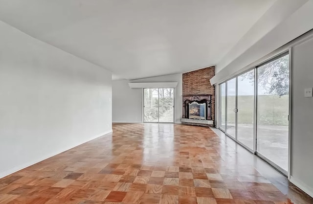 unfurnished living room featuring brick wall, vaulted ceiling, a fireplace, and light parquet floors