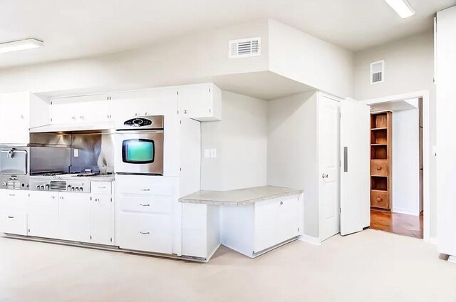 kitchen with white cabinets, stainless steel oven, and light hardwood / wood-style floors