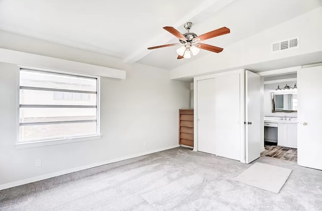 unfurnished bedroom featuring a closet, ceiling fan, ensuite bath, light carpet, and lofted ceiling with beams