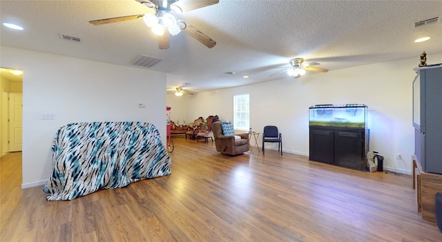 living room featuring hardwood / wood-style flooring, ceiling fan, and a textured ceiling