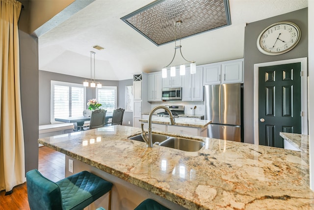 kitchen featuring white cabinets, sink, hanging light fixtures, light stone counters, and stainless steel appliances